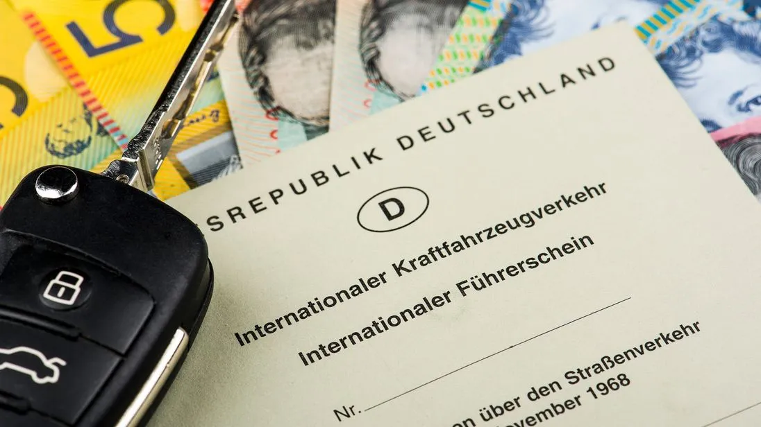 Internationaler Führerschein der Bundesrepublik Deutschland liegt auf mehreren Geldscheinen neben einem Autoschlüssel.