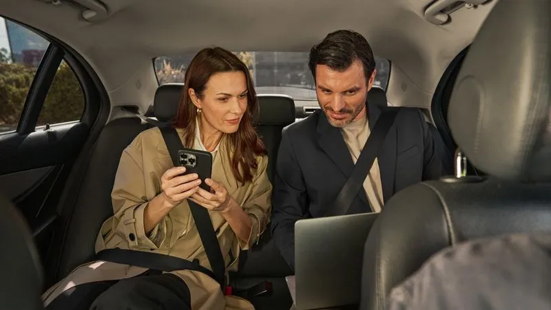 Geschäftsreisende im Taxi mit Smartphone und Laptop
