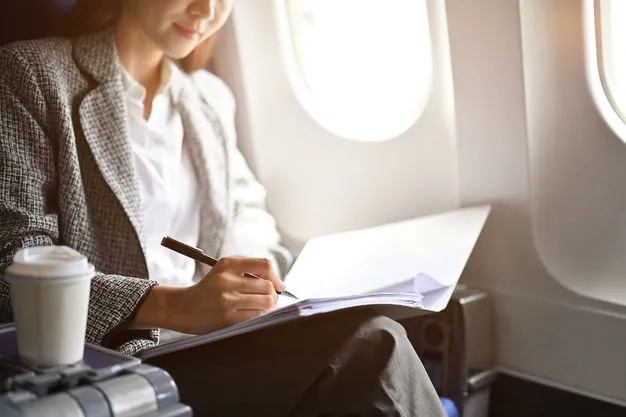 Eine Frau sitzt im Flugzeug in einem Meeting und macht sich in ihrer Mappe mit einem Stift Notizen.