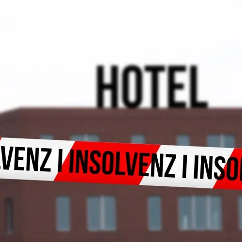 Hotel im Hintergrund und vorne ein rot-weißes Absperrband mit den Worten "Insolvenz".