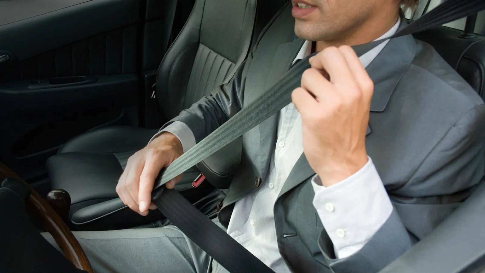 Ein Business-Mann im Anzug schnallt sich in seinem Wagen an.