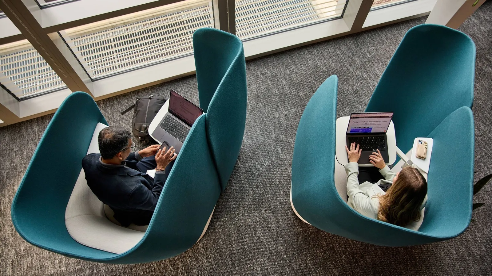 Zwei Personen sitzen mit Laptops in abgeschirmten Sesseln.