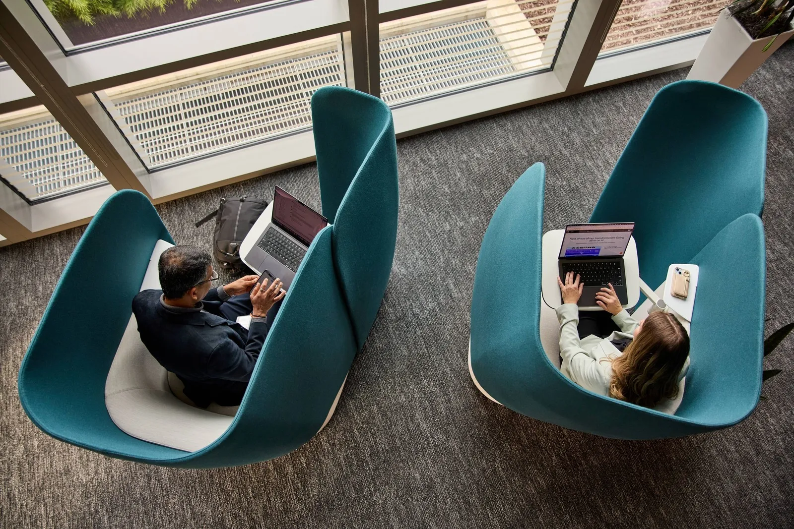 Zwei Personen sitzen mit Laptops in abgeschirmten Sesseln.