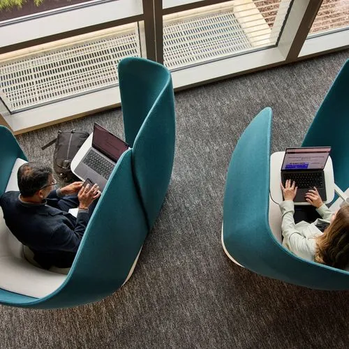Zwei Personen sitzen mit Laptops in abgeschirmten Sesseln.
