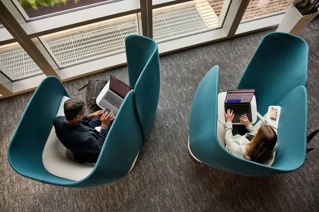 Zwei Personen sitzen mit Laptops in abgeschirmten Sesseln.