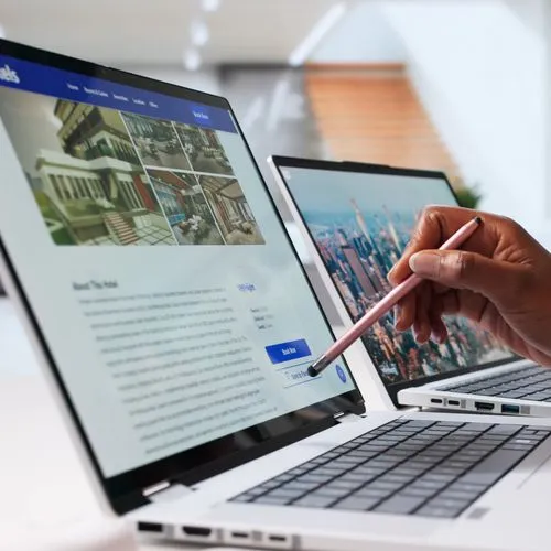 Eine Hand zeigt mit einem Stift auf einen Laptop. Auf dem Laptop ist eine Hotel-Buchungsseite geöffnet.