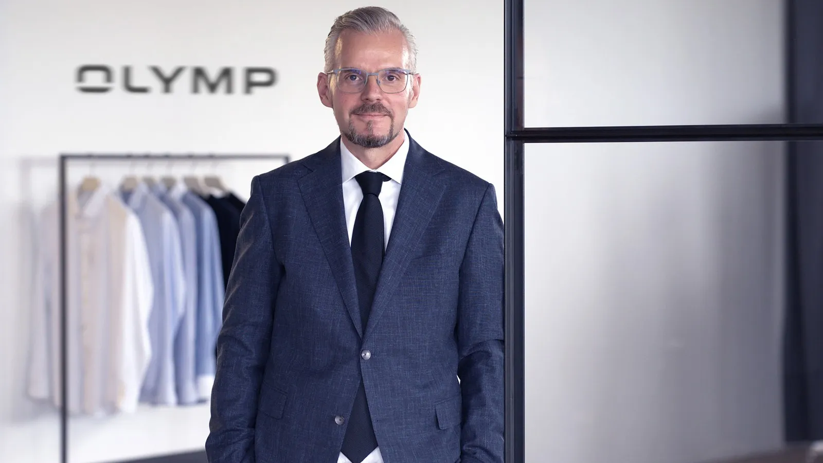 Johann Trischberger, COO bei Olymp, trägt einen dunkelblauen Anzug und schaut in die Kamera.
