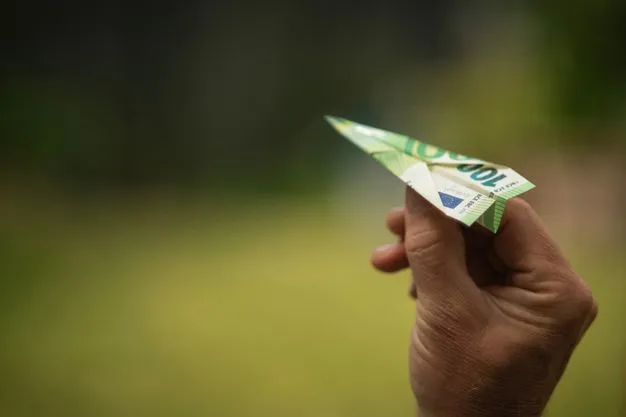 Eine Hand hält ein aus einem 100-Euro-Schein gefaltetes Papierflugzeug vor unscharfem Hintergrund.