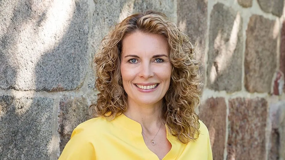 Porträt von Maren Ulbrich, Diplom-Ökonomin und zertifizierte Unternehmensnachfolge-Beraterin, vor einer Steinwand.