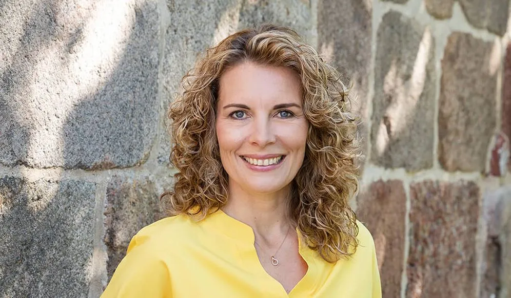 Porträt von Maren Ulbrich, Diplom-Ökonomin und zertifizierte Unternehmensnachfolge-Beraterin, vor einer Steinwand.