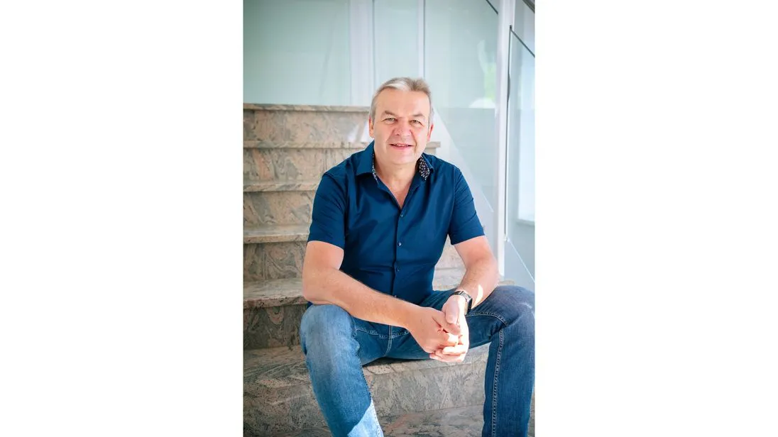 Reinhard Peter sitzt in einem blauen Hemd auf einer Treppe und schaut in die Kamera.