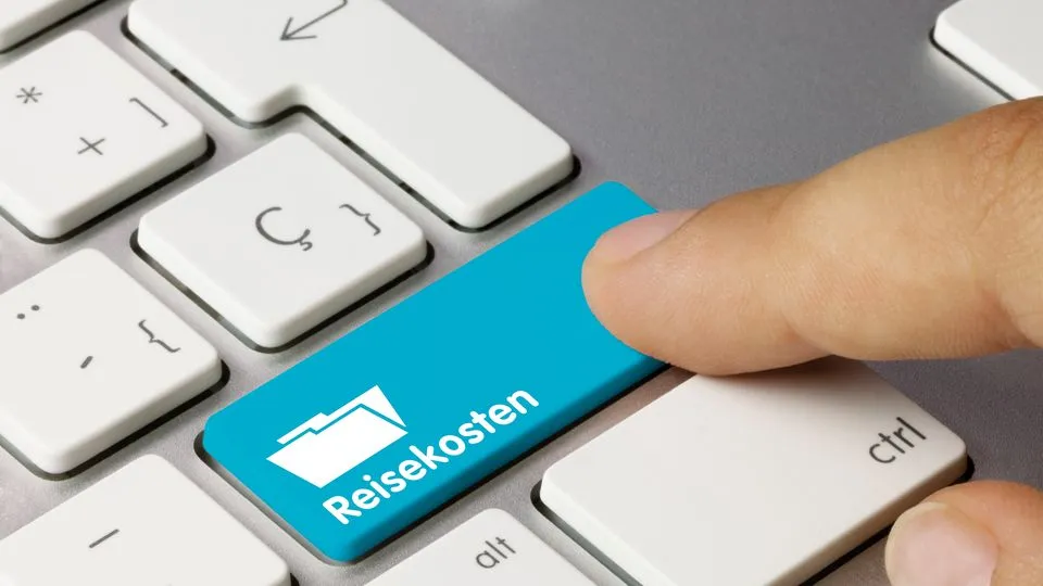 Finger drückt auf einer Computertastatur eine blaue Taste mit der Aufschrift „Reisekosten“.