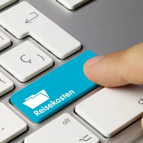 Finger drückt auf einer Computertastatur eine blaue Taste mit der Aufschrift „Reisekosten“.