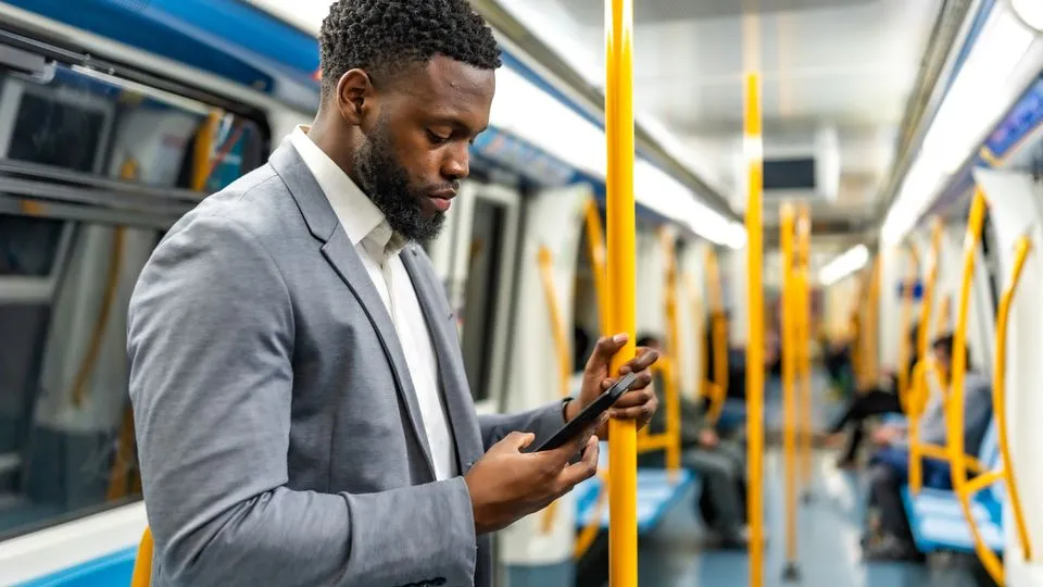 Geschäftsreisender steht in einer U-Bahn und blickt auf sein Smartphone.