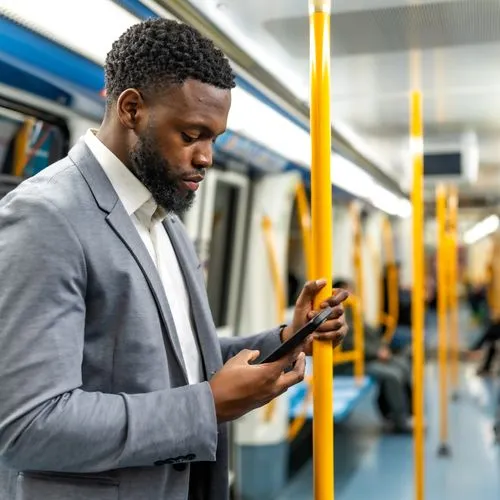 Geschäftsreisender steht in einer U-Bahn und blickt auf sein Smartphone.