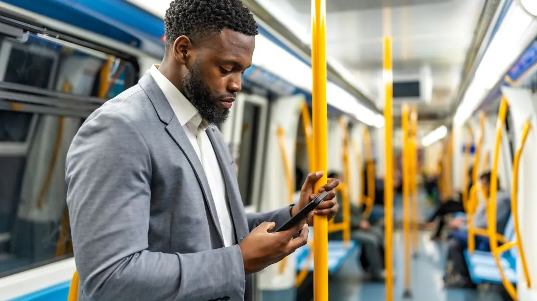 Geschäftsreisender steht in einer U-Bahn und blickt auf sein Smartphone.
