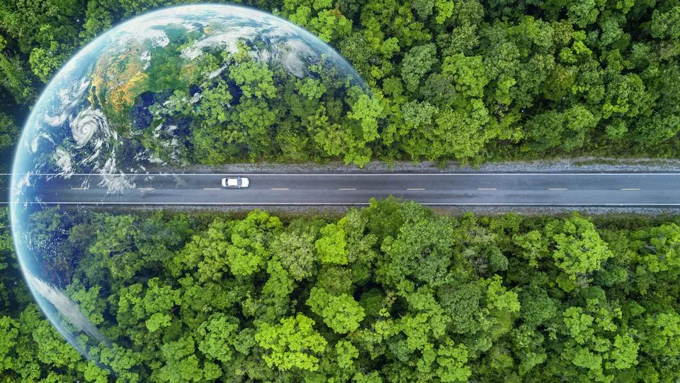 Eine Aufnahme von einem Auto, dass auf einer langen Straße fährt, in der Vogelperspektive. Die Straße ist umgeben von grünen Wäldern.