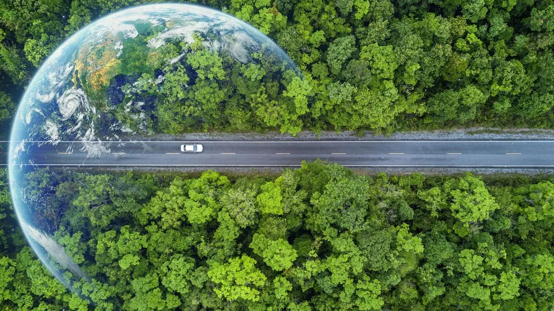 Eine Aufnahme von einem Auto, dass auf einer langen Straße fährt, in der Vogelperspektive. Die Straße ist umgeben von grünen Wäldern.